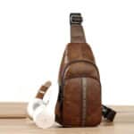 Petit sac à dos bandoulière en cuir posé sur un table en bois avec un casque audio blanc.