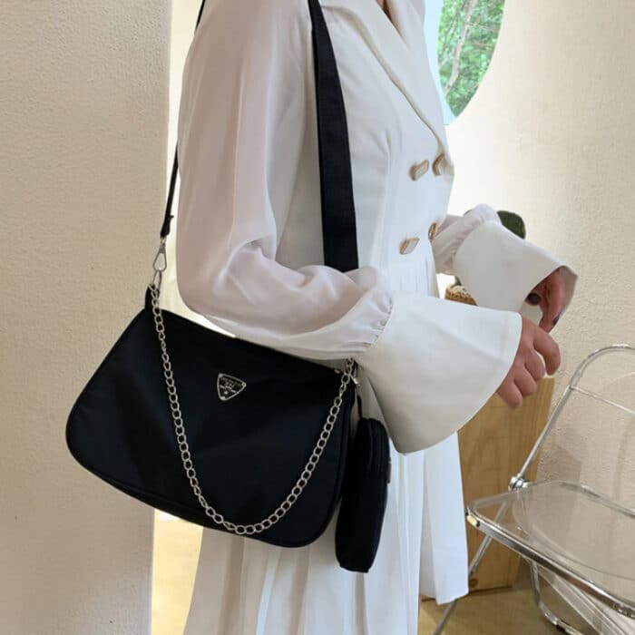 Femme en chemise blanche de profil portant un sac à main en bandoulière noir avec une chaîne