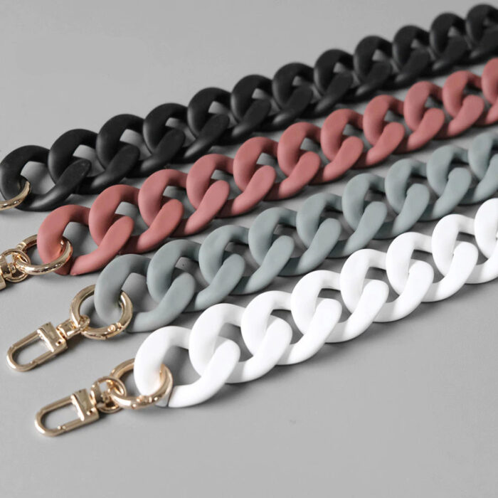 4 chaines pour sac colorées en blanc, noir, bleu et rose avec attaches dorées sur fond gris