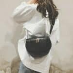 Femme de dos portant une chemise blanc avec un sac noir en cuir à bandoulière