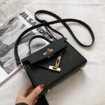 Petit sac à main bandoulière à fermoir original à l'avant. Tenu par un pouce au vernis rouge.