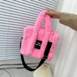 Photo d'un sac à main à bandoulière en fausse fourrure rose tenue par une main devant un volet.