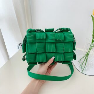 Photo d'un sac pochette à bandoulière en cuir synthétique texturé vert tenu dans une main au dessus du sol.