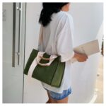 Photo d'une femme portant un sac cabas en toile vert en bandoulière devant une porte en verre