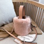 Photo d'un sac seau à bandoulière en fausse fourrure et cuir synthétique rose posé su une chaise