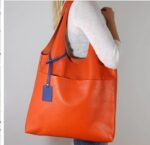 Sac large orange porté par une femme blonde au t-shirt blanc