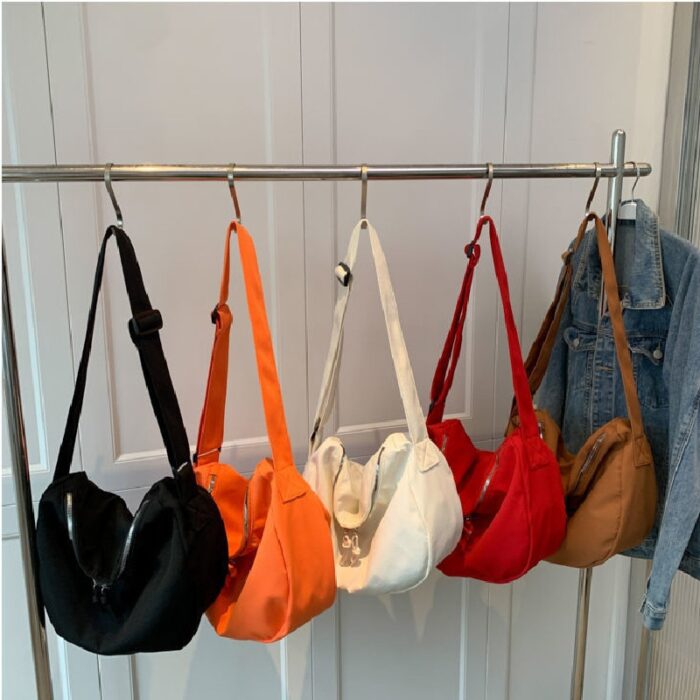 même modéle de sac bandoulière noir, orange, blanc, rouge et marron accrochés à des tringles