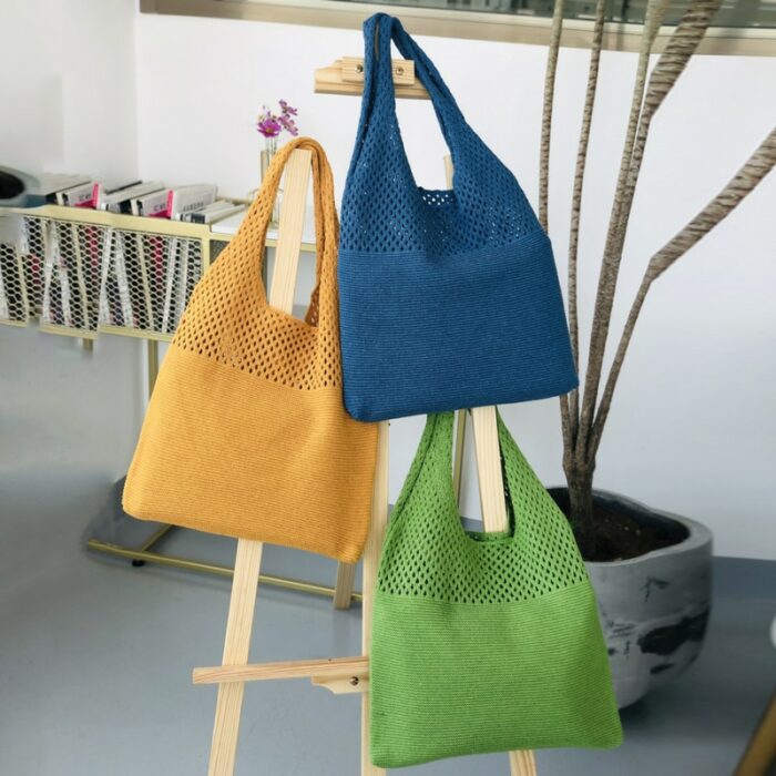 Dans une pièce moderne à la décoration plutôt minimaliste, on voit un portant en bois sur lequel sont suspendus des sacs tricotés. Ils sont à bandoulière et de trois couleurs différentes. Un jaune, un bleu, une vert.