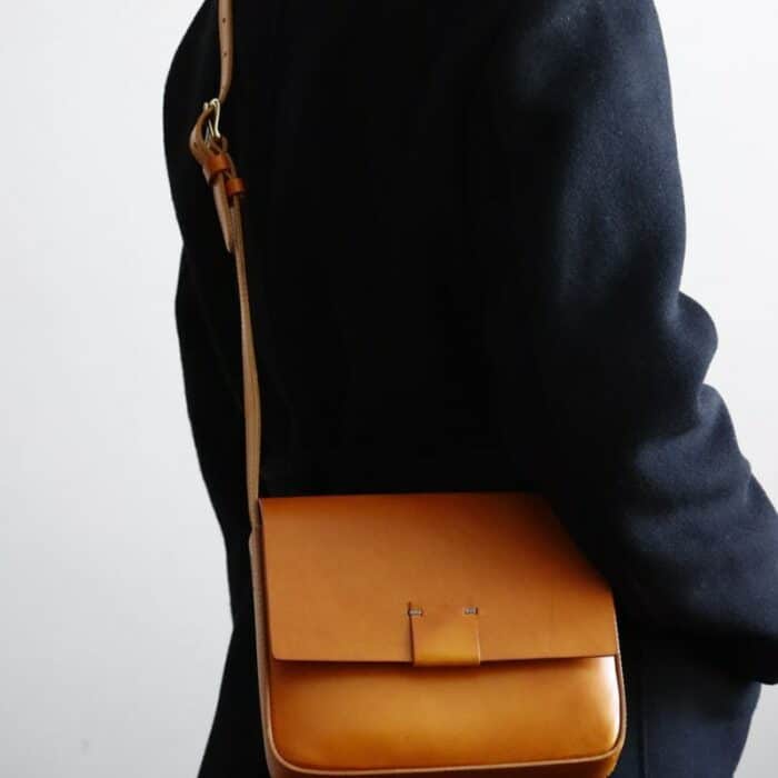Photo d'un sac pochette bandoulière en cuir camel porté par une personne avec un manteau noir