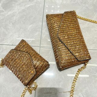 Photo de deux sac pochette bandoulière en strass dorés posé sur un carrelage gris.