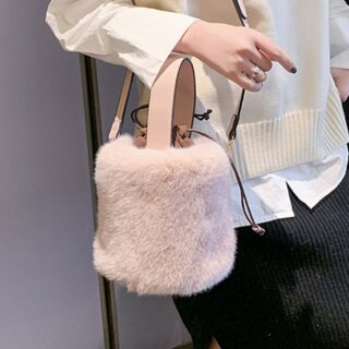 Petit sac à main en forme de seau en fourrure rose avec bandoulière. Porté par jeune femme à la chemise blanche.