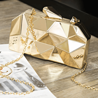 Photo d'un sac pochette à bandoulière en 3D doré posé sur une table en bois avec un magazine