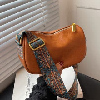 Petit sac bandoulière effet cuir uni marron avec bandoulière à motifs dans main de femme