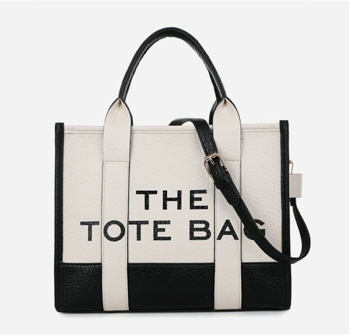 Sac bandoulière type tote bag noir et blanc avec inscription "the tote bag" sur fond blanc.